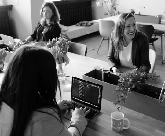 ladies in an office talking smiling and typing a computer